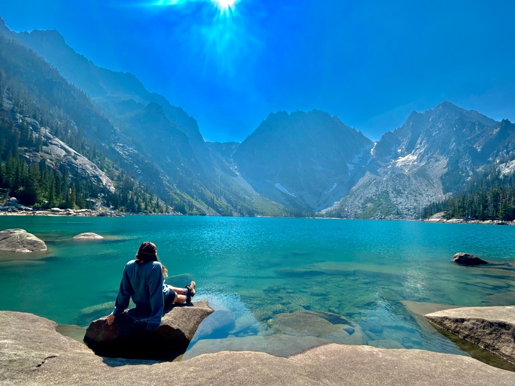 girl looking at out a blue lake with mountains in the background