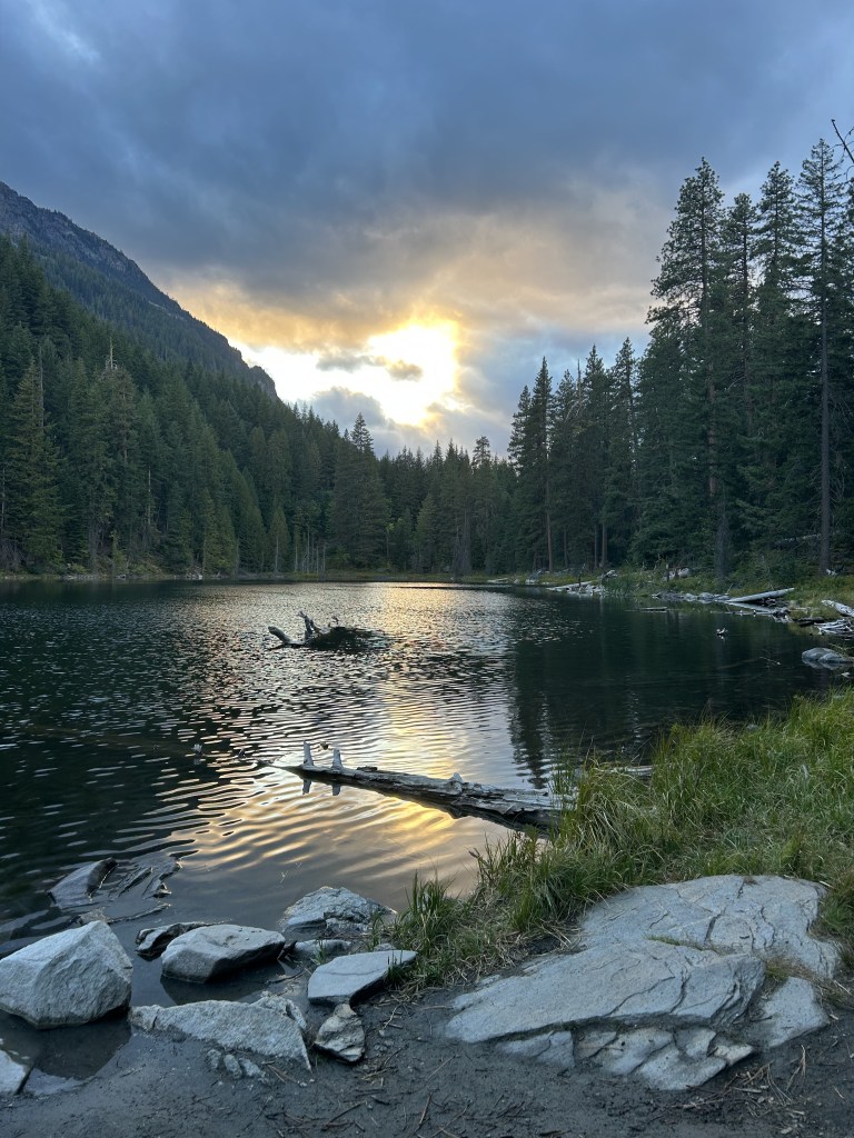 lake surrounded by forest with the sun setting in the background